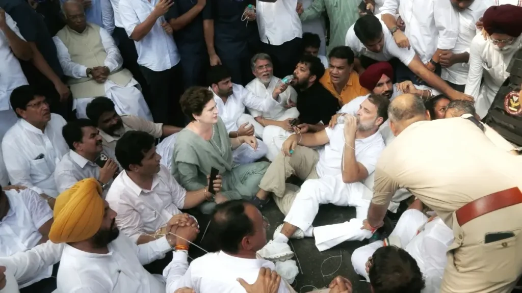 রাহুল গান্ধী ও প্রিয়াঙ্কা গান্ধী সমর্থকদের সঙ্গে সড়কে অবস্থান কর্মসূচিতে বসে আছেন, তাদের চারপাশে দিল্লি পুলিশের সদস্যরা অবস্থান নিয়েছেন