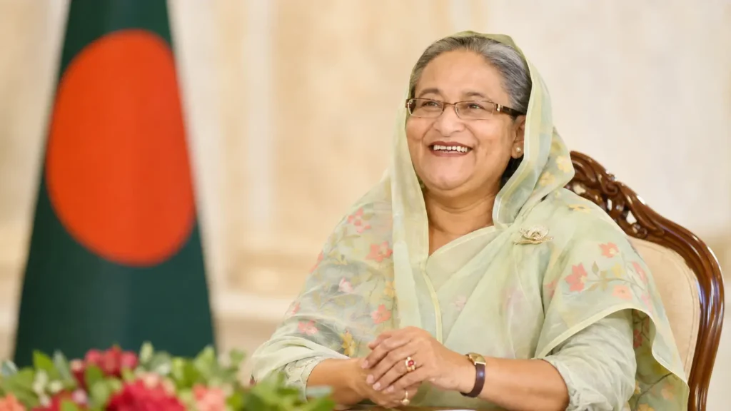 বাংলাদেশের সাবেক প্রধানমন্ত্রী শেখ হাসিনার হাস্যোজ্জ্বল আনুষ্ঠানিক প্রতিকৃতি, পটভূমিতে বাংলাদেশের জাতীয় পতাকা