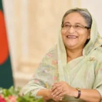 বাংলাদেশের সাবেক প্রধানমন্ত্রী শেখ হাসিনার হাস্যোজ্জ্বল আনুষ্ঠানিক প্রতিকৃতি, পটভূমিতে বাংলাদেশের জাতীয় পতাকা