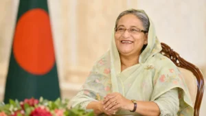 বাংলাদেশের সাবেক প্রধানমন্ত্রী শেখ হাসিনার হাস্যোজ্জ্বল আনুষ্ঠানিক প্রতিকৃতি, পটভূমিতে বাংলাদেশের জাতীয় পতাকা
